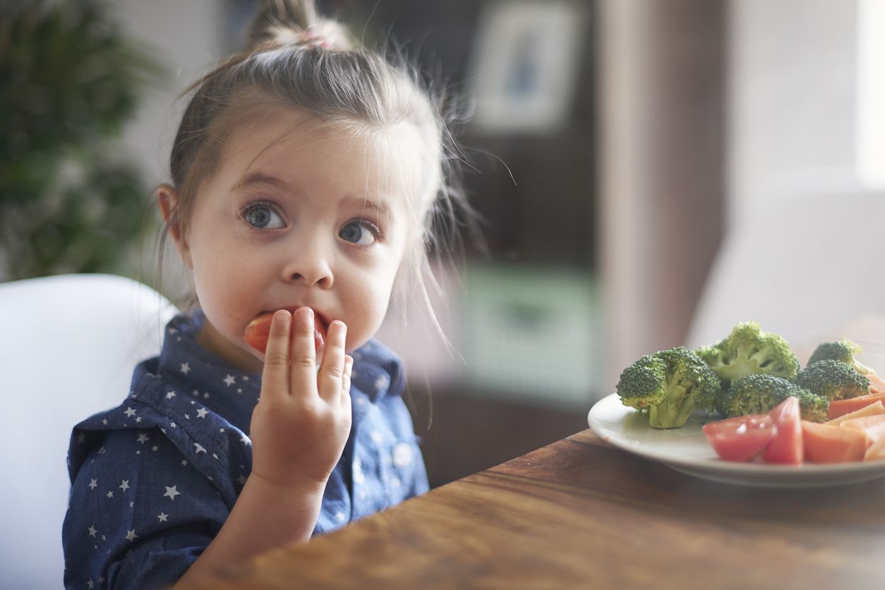Una nena menja verdures sentada en una taula